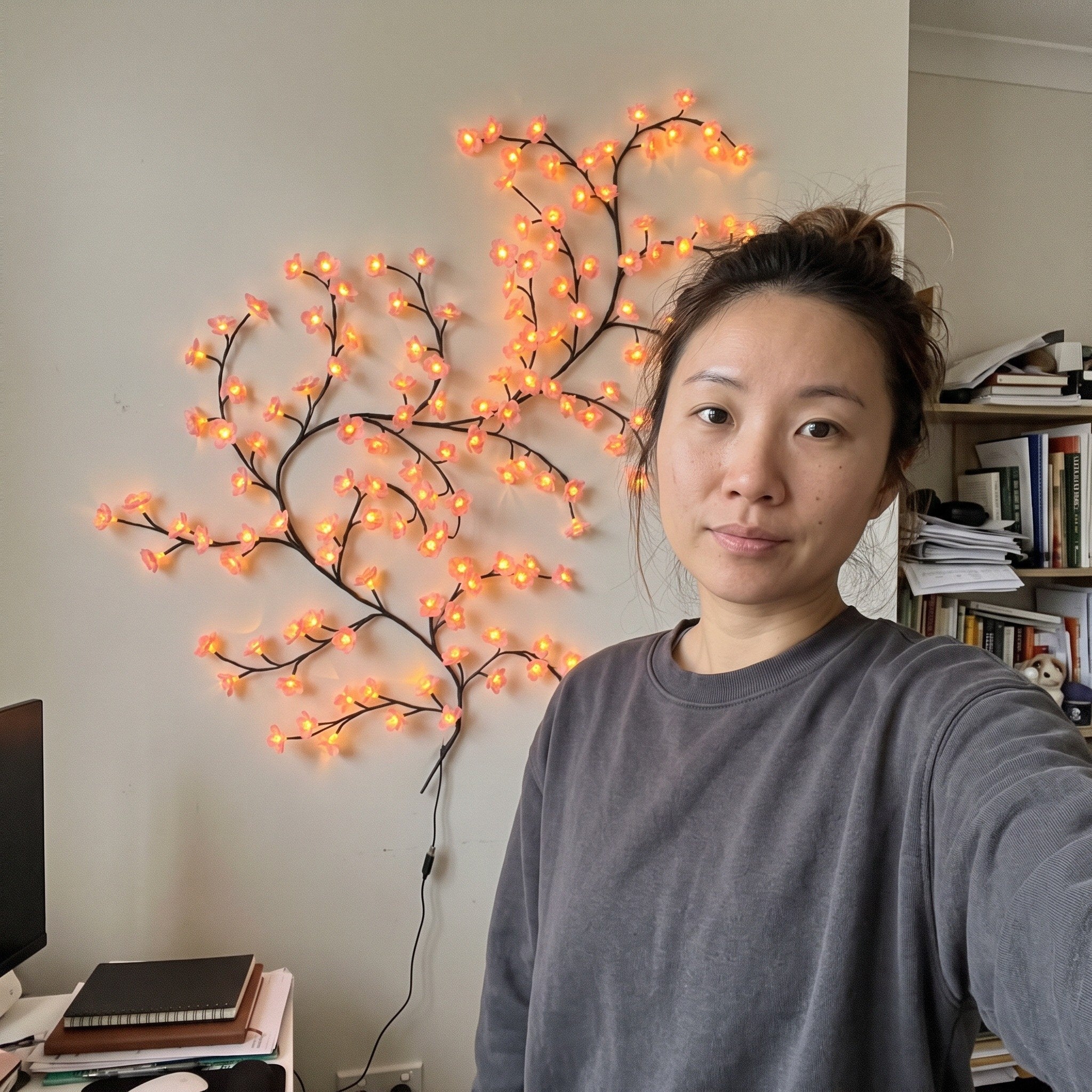 Woman taking a study selfie by pink blossom vine lights